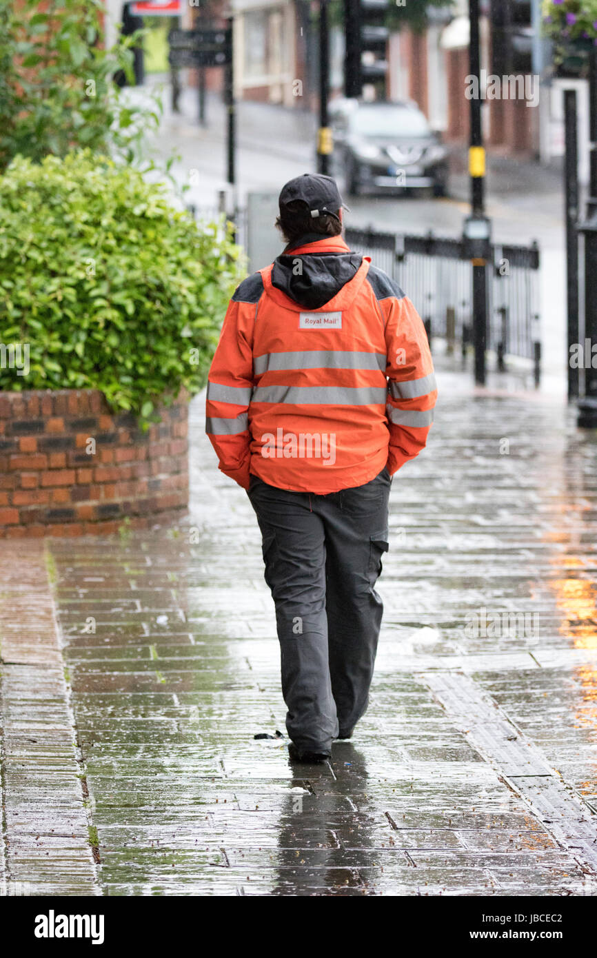 Post Officer Arbeiter nach Hause nach einer Nachtschicht wandern im Regen auf einer nassen Straße in der Stadt von Schimmel, Flintshire, Wales, Großbritannien Stockfoto