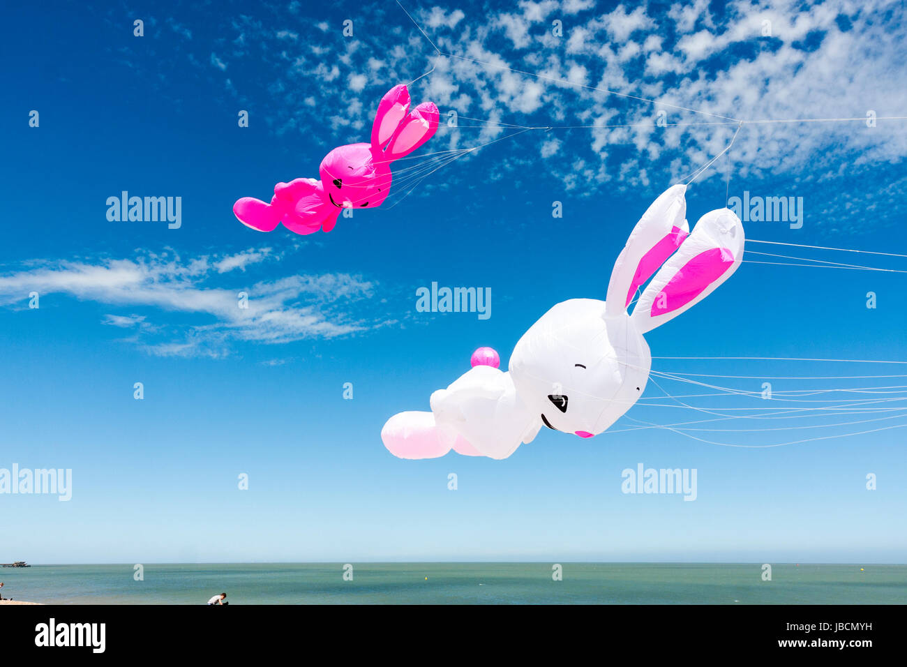 Zwei bunny geformte aufgeblasen Drachen, eine weiße, rosa, Fliegen gegen den blauen Himmel. Meer unter. Teil des Walmer Stadt Drachenfliegen Festival. Stockfoto