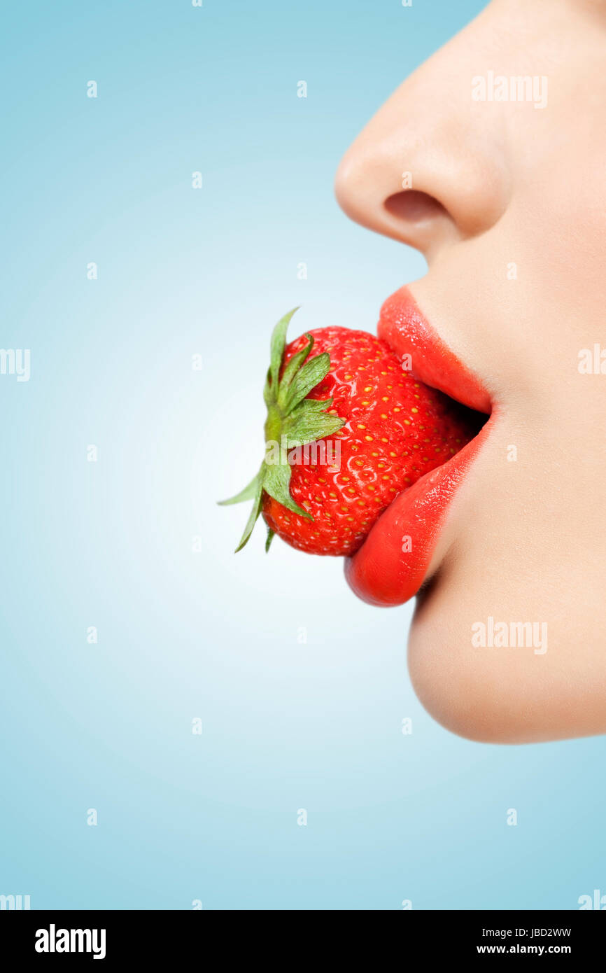 Eine kreative Porträt von einem schönen weiblichen Gesicht hält eine rote Reife Erdbeere in ihren sexy Mund. Stockfoto