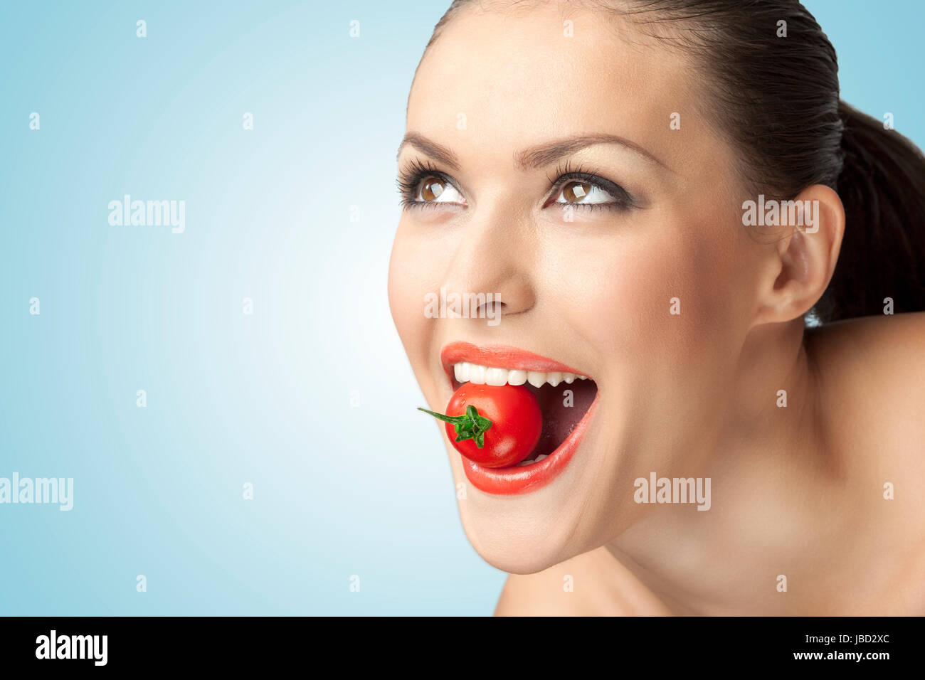 Ein kreativer Porträt eines schönen Mädchens mit einer Kirschtomate sexuell in ihrer Zähne. Stockfoto