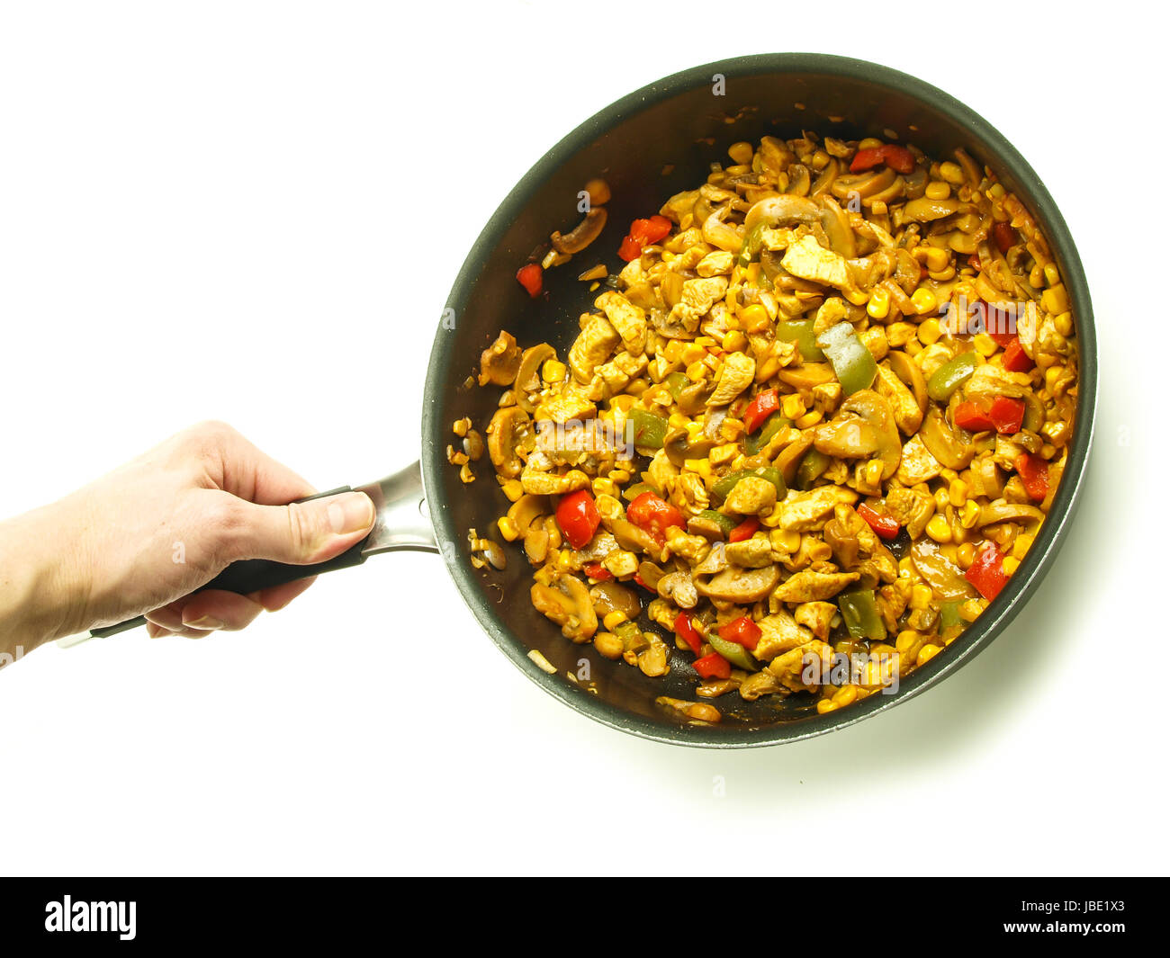 Braten Pfanne mit Huhn mit Curry, Paprika und Mais statt von einem männlichen Koch auf weißem Hintergrund Stockfoto