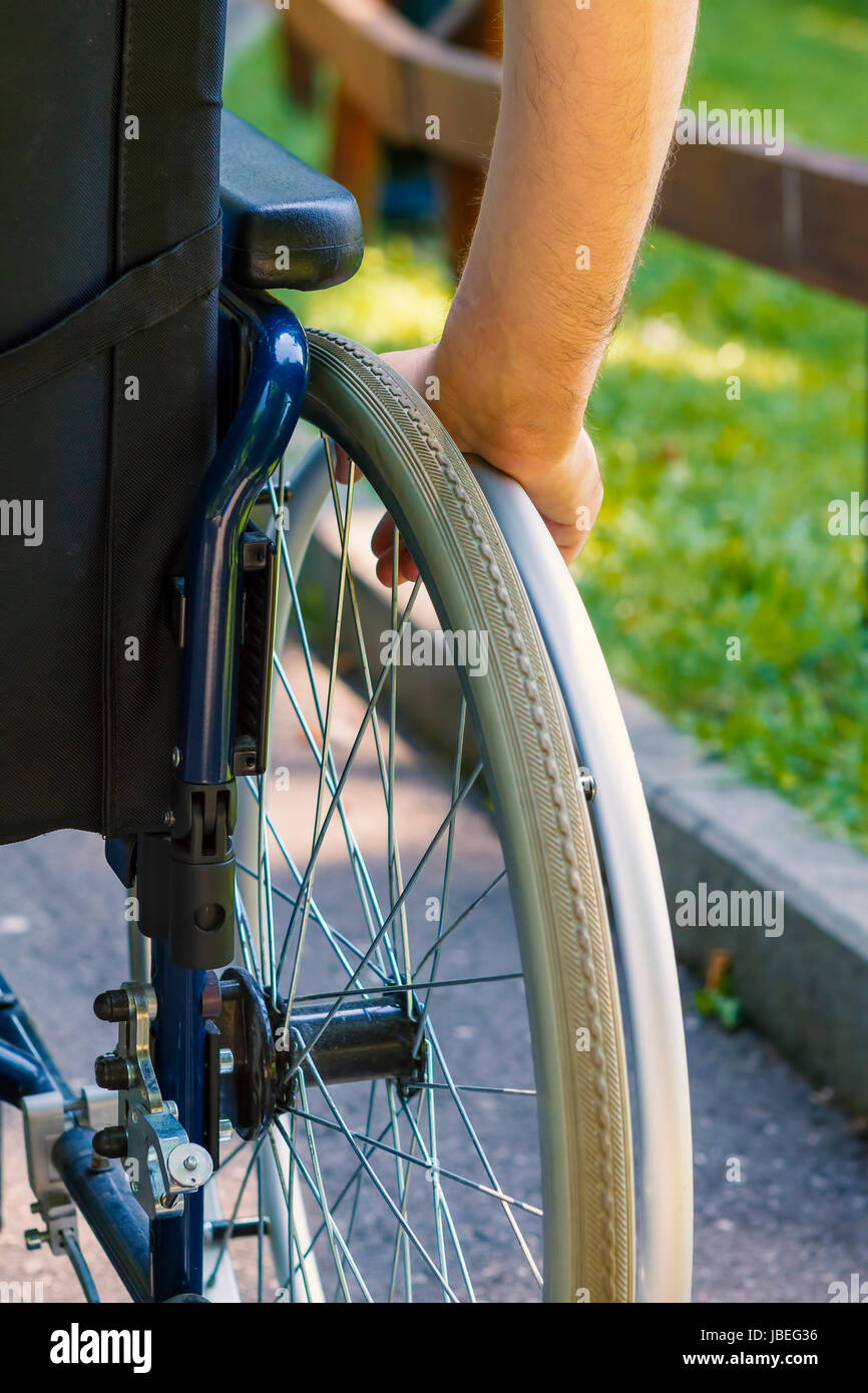 Hand des jungen Mannes auf dem Rad des Rollstuhls im Stadtpark Stockfoto
