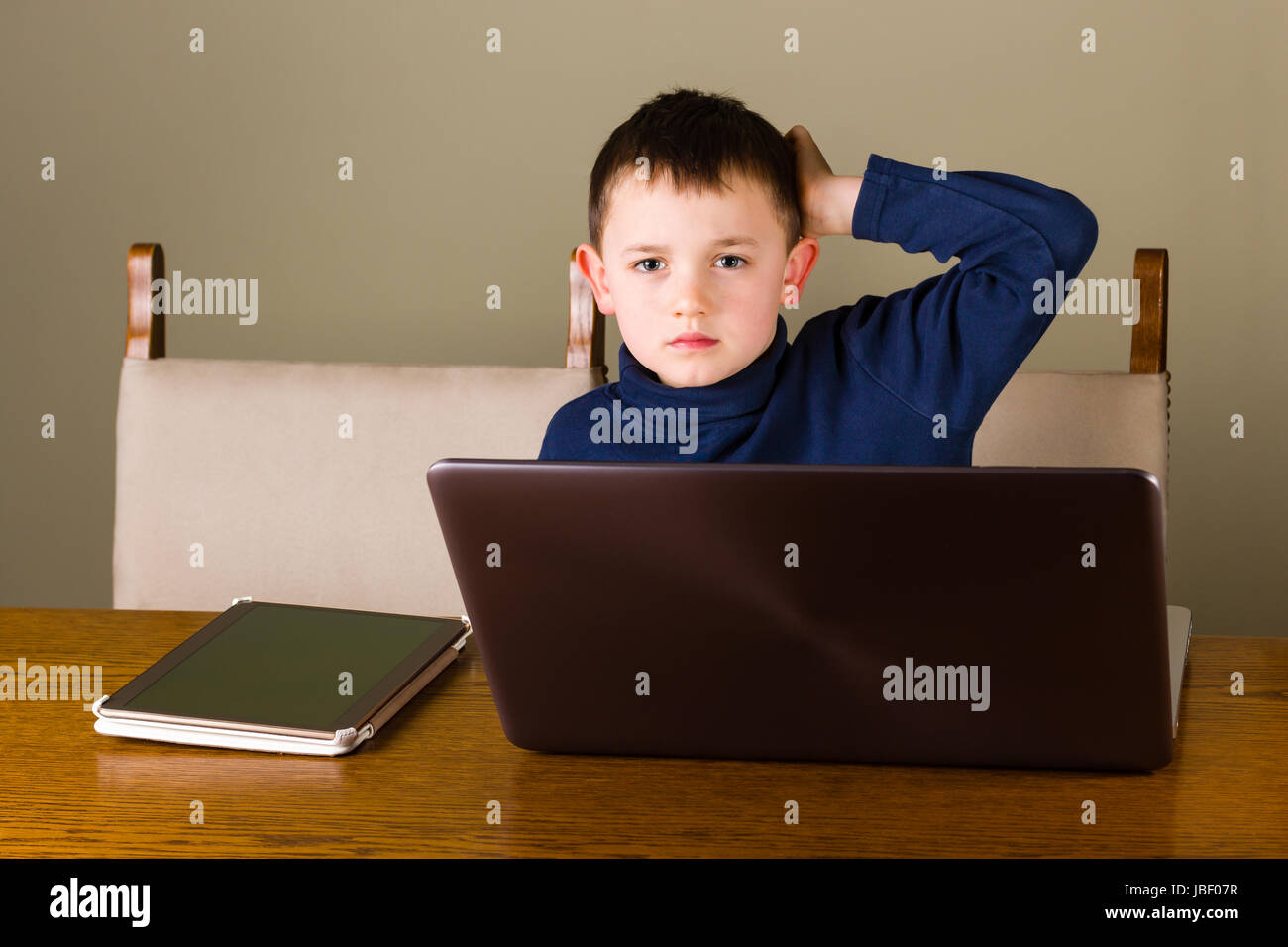 Niedliche kleine Junge auf neue Technologie, sitzt hinter dem Laptop und Tablet pc zu Hause, auf der Suche konzentriert. Stockfoto