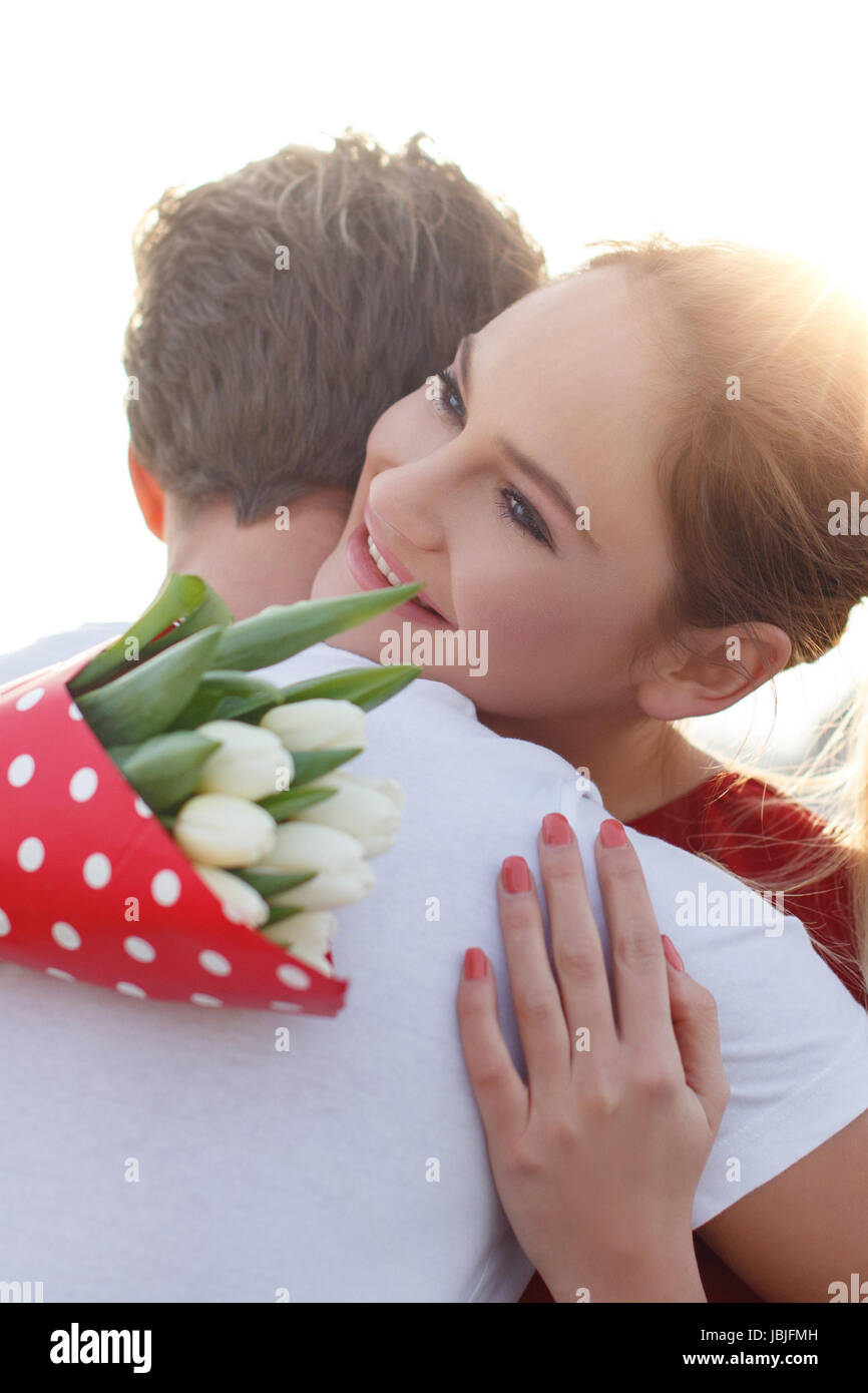 Glückliches junges Paar am ersten Tag umarmen mit Blumenstrauß Stockfoto