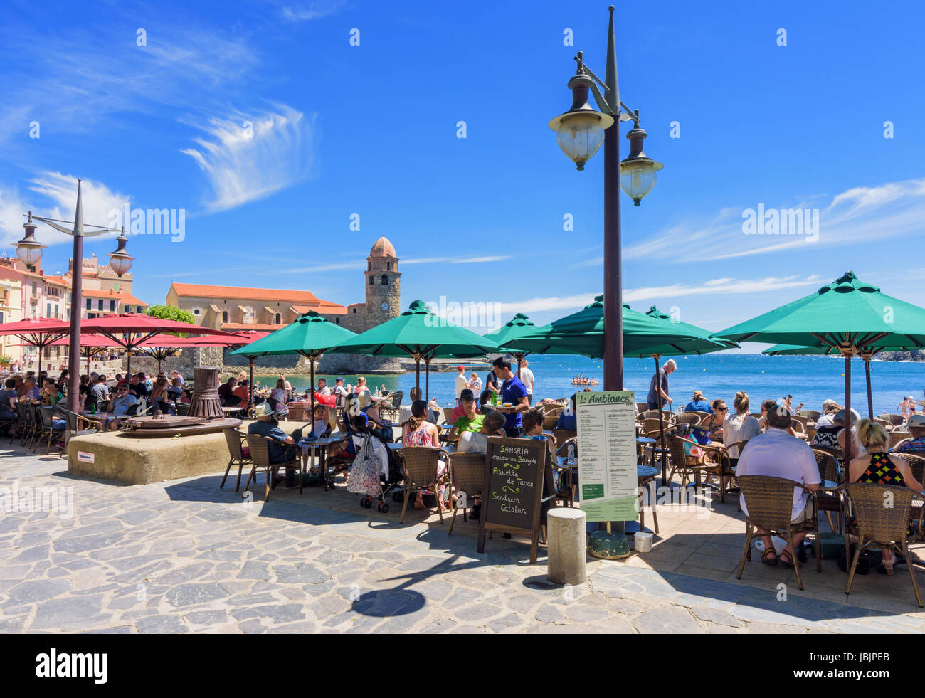 Belebten Café gesäumten Uferpromenade von Collioure Stadt überragt vom Glockenturm der Kirche von Notre Dame des Anges, Collioure, Côte Vermeille, Frankreich Stockfoto