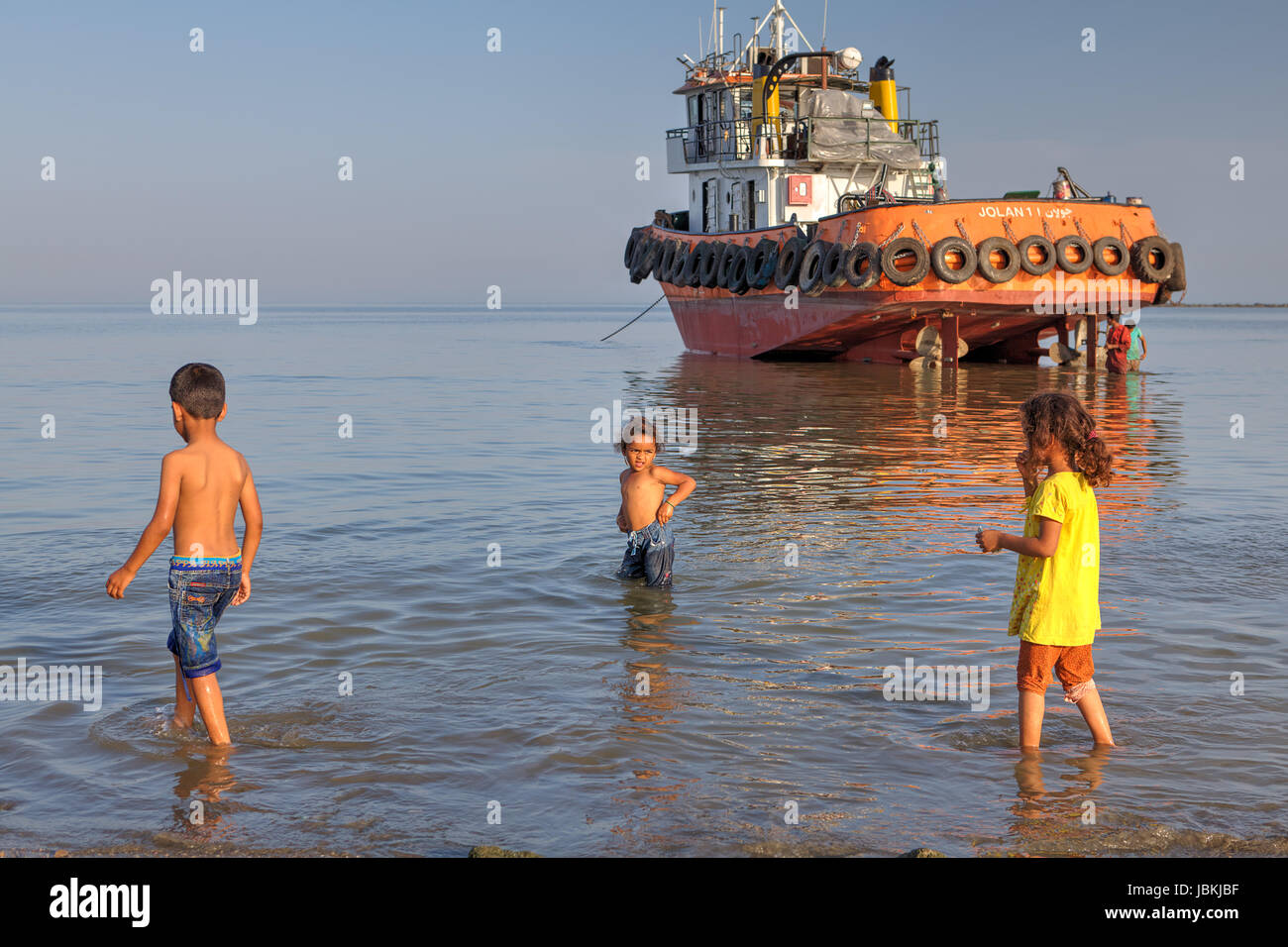 Bandar Abbas, Provinz Hormozgan, Iran - 16. April 2017: drei Kinder von etwa 7 Jahre alt, spielen im Wasser gegen ein Schlepper auf Grund gelaufen. Stockfoto