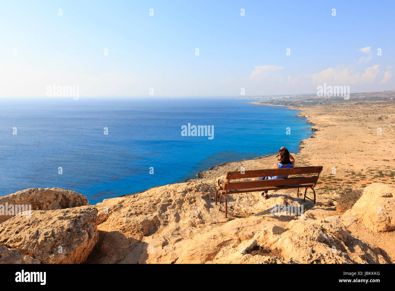 Eine einsame Frau sitzen auf einer Bank am Kap Greco Klippe Top Blick über das Mittelmeer in Richtung Ayia Napa in der Ferne. Zypern. Stockfoto