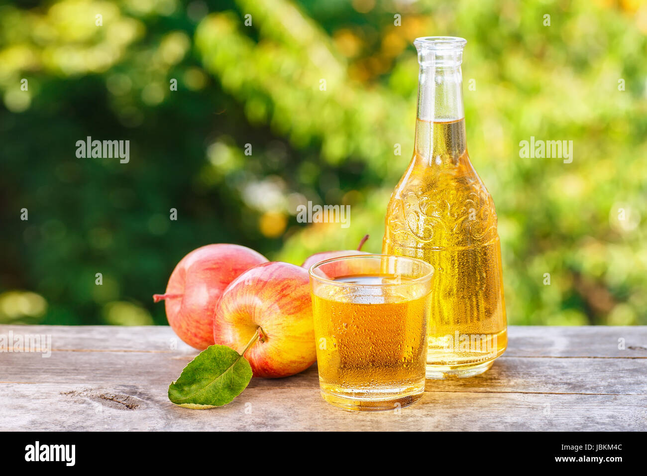 Apfelwein oder Saft im Glas mit Reife frische Äpfel auf Holztisch mit grünen natürlichen Hintergrund. Horizontalen Schuss mit Textfreiraum. Erfrischende Sommer Stockfoto
