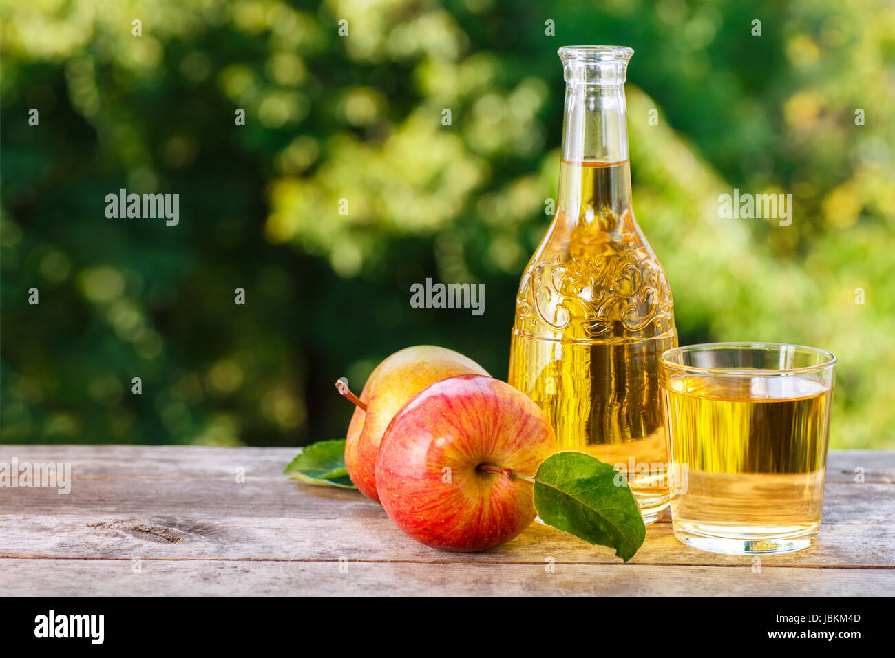 Apfelwein oder Saft im Glas mit Reife frische Äpfel auf Holztisch mit grünen natürlichen Hintergrund. Horizontalen Schuss. Sommergetränk Stockfoto