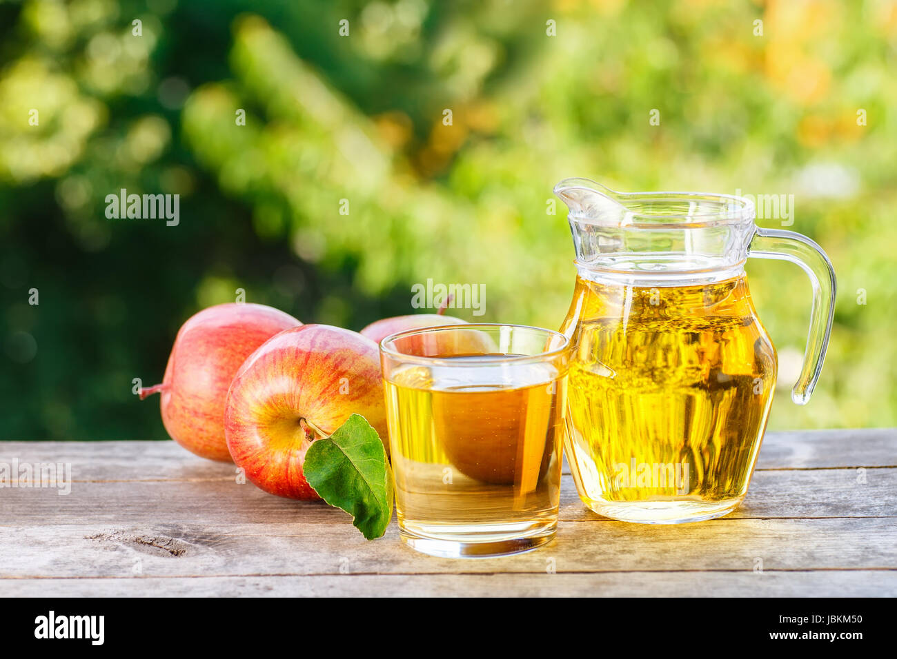 Apfelsaft aus Glas und frische Äpfel auf Holztisch mit grünen Bokeh Hintergrund. Horizontalen Schuss. Sommergetränk Stockfoto
