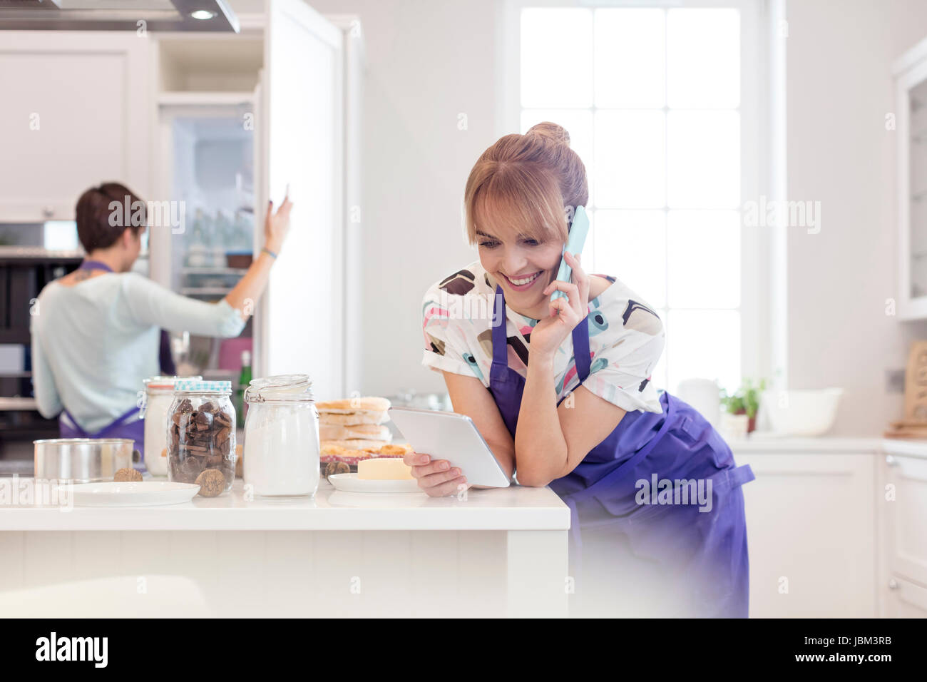 Weibliche Caterer Backen und arbeiten in der Küche, reden über Handy und mit digital-Tablette Stockfoto