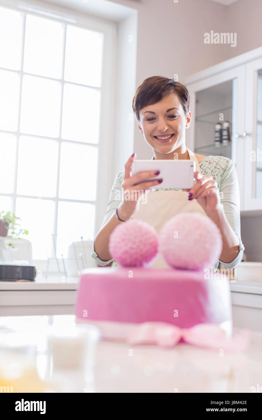 Weibliche Caterer mit Handykamera fotografiert rosa Hochzeitstorte in Küche Stockfoto