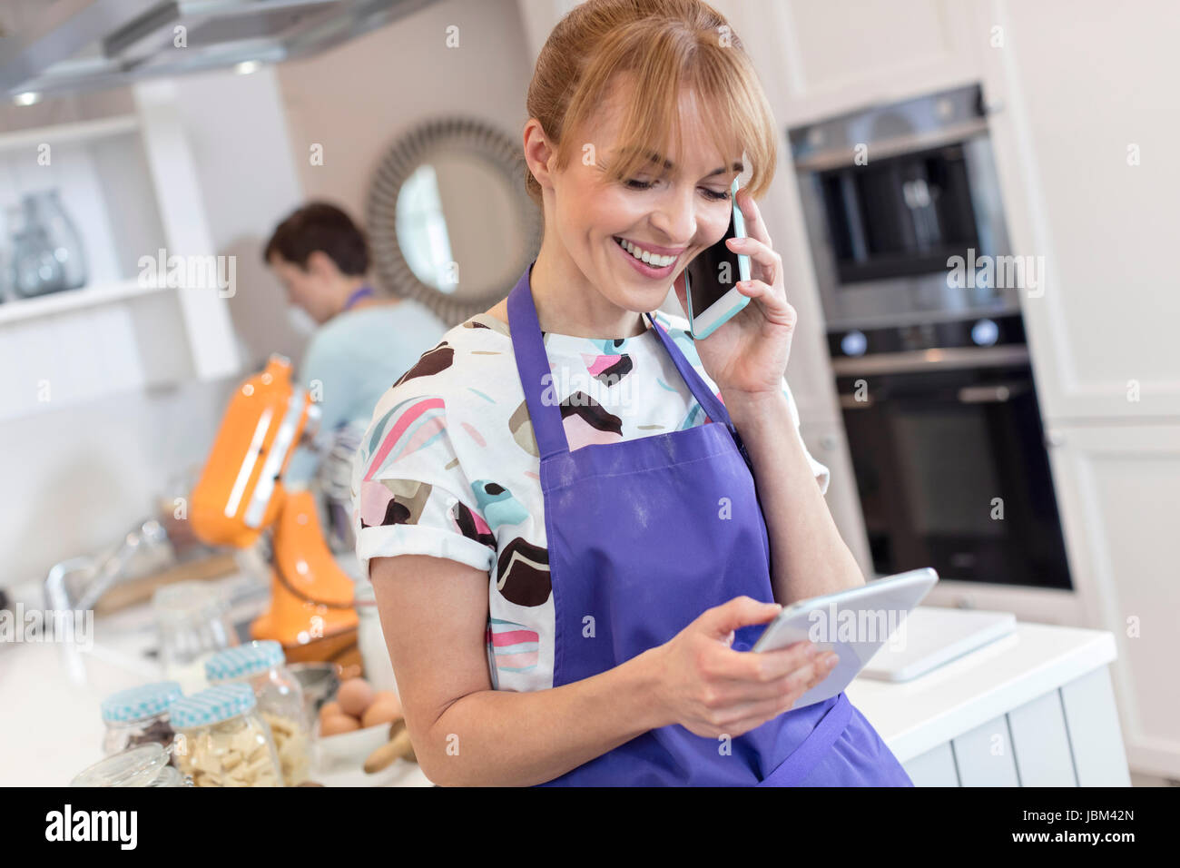 Lächelnde Caterer arbeiten, reden über Handy und Verwendung von digital-Tablette in Küche Stockfoto