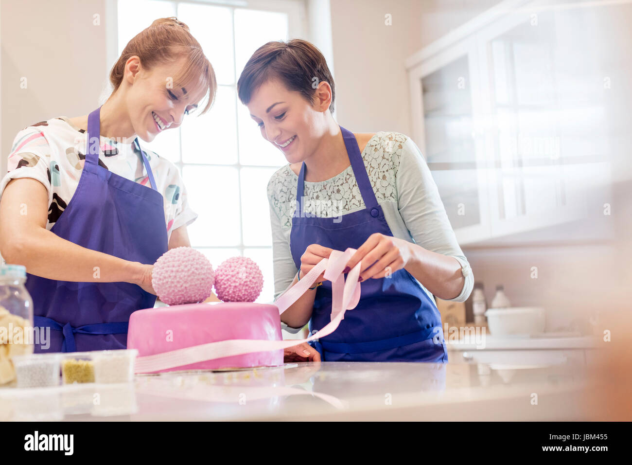 Weibliche Caterer Veredelung rosa Hochzeitstorte in Küche Stockfoto