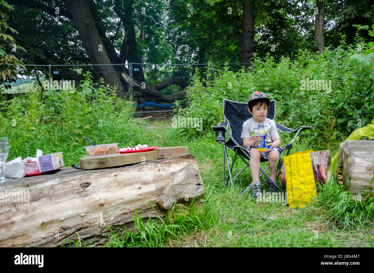 Ein junger Bot sitzt in einem Klappstuhl auf einem Campingplatz und Snjoys einen Drink. Stockfoto