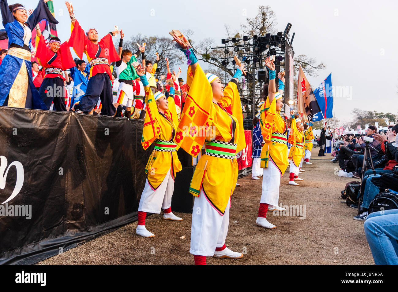 Hinokuni Yosakoi Dance Festival in Kumamoto, Japan. Junge Tänzerinnen in Gelb traditionelle Yukata Jacken, tanzen vor der Bühne und Publikum. Stockfoto