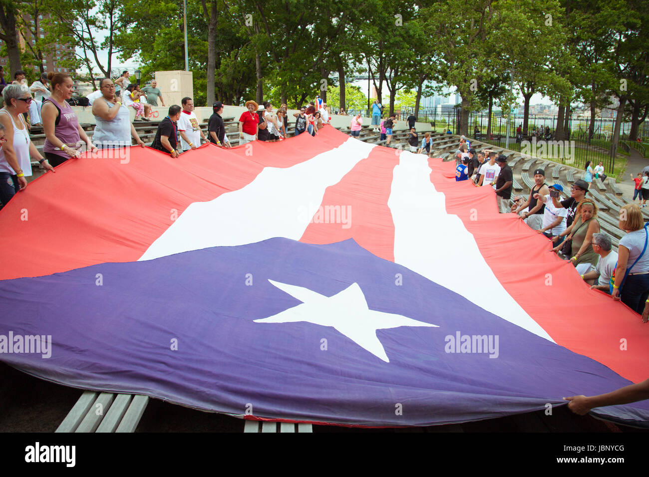 Eine riesige Puerto-ricanische Flagge wird während einer öffentlichen Demonstration von einer Menge hochgehalten, die Solidarität, Patriotismus und kulturelle Identität zeigt. Stockfoto