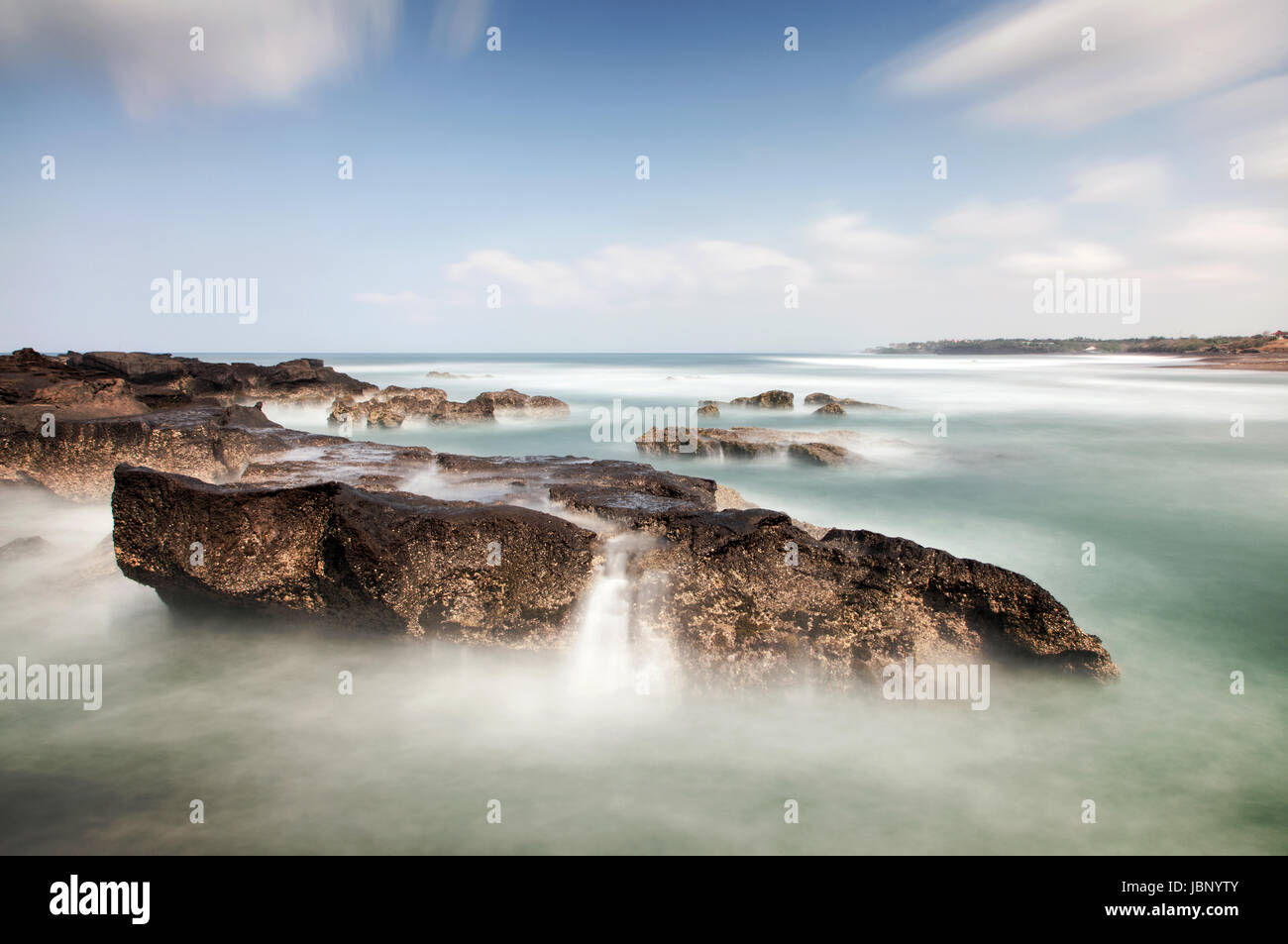 Lange Exposition Seelandschaft mit Mini-Wasserfälle, die auf einem Felsen im Meer an der balinesischen Küste mit beeindruckendem Wolken und herrliche Panorama-Aussicht Stockfoto