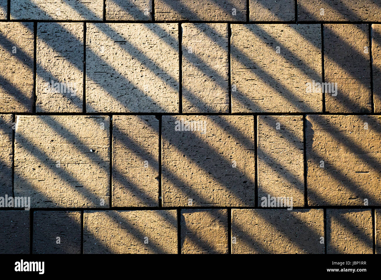 Pflastersteine aus Beton auf Boden beleuchtet durch Sonne und mit Reling Schattenlinien schräg gelegt Stockfoto
