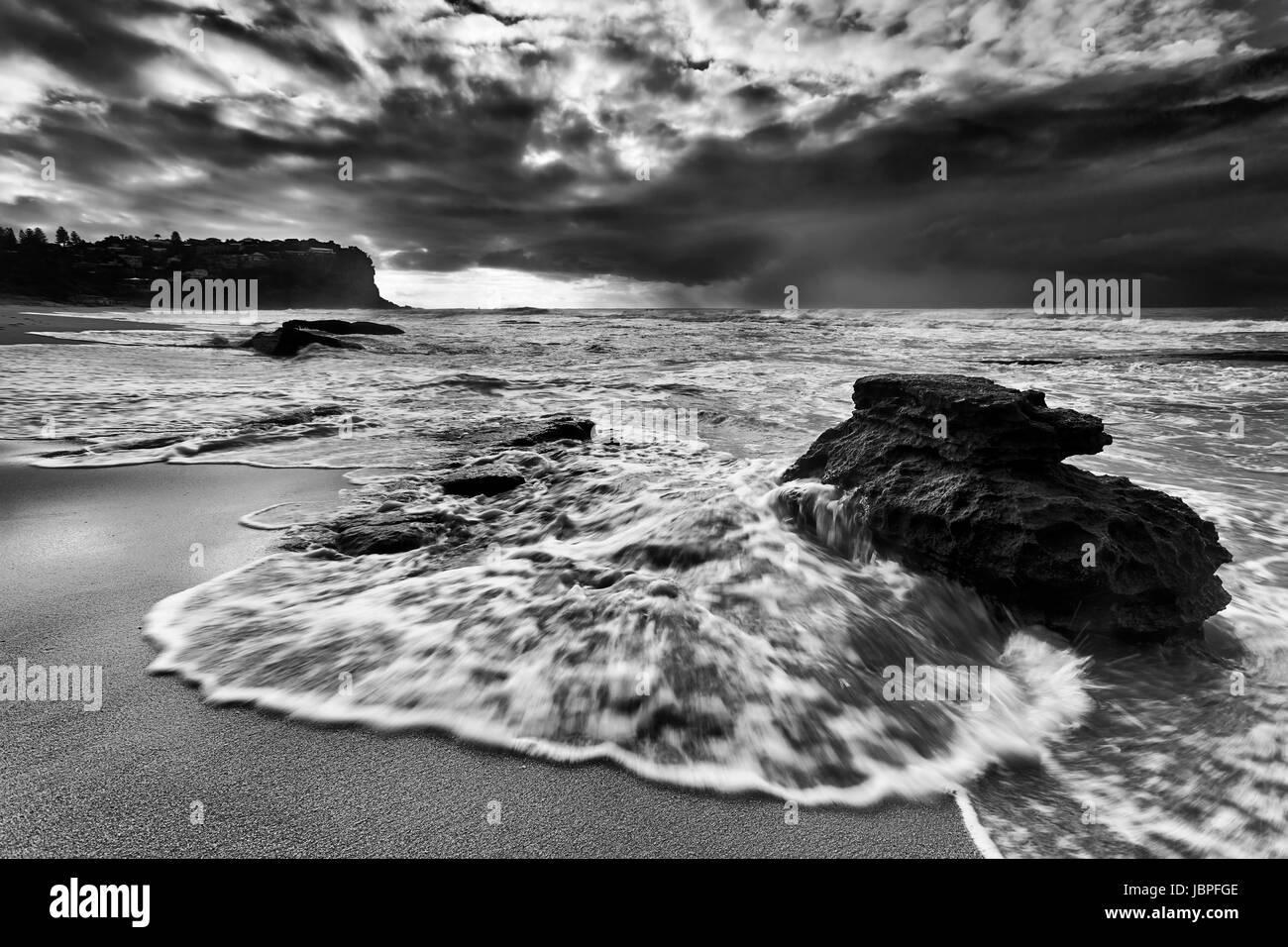 Schnell fließende Flutwelle überflutet Sandstein Felsen am Strand von Sydney Nord-Sandstrände der Bungan bei Sonnenaufgang bei stürmischem Wetter. Stockfoto