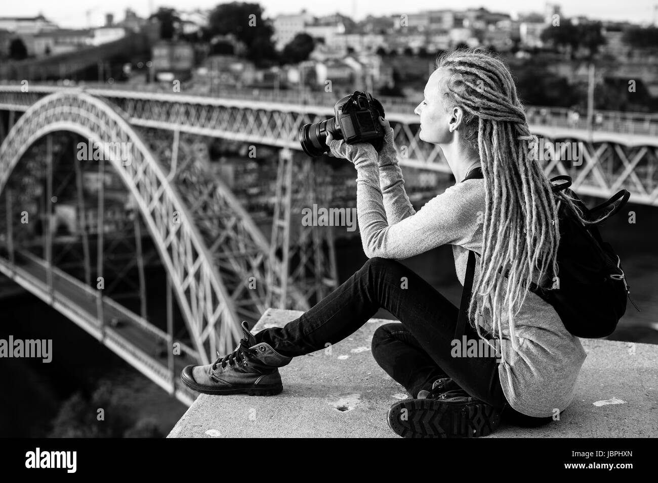 Junge schöne Frau mit Dreadlocks und eine Kamera sitzt Fotografieren von einem Dom Luis ich in alten Porto, Portugal zu überbrücken. Tourismus und Reisen, schwarz und Stockfoto