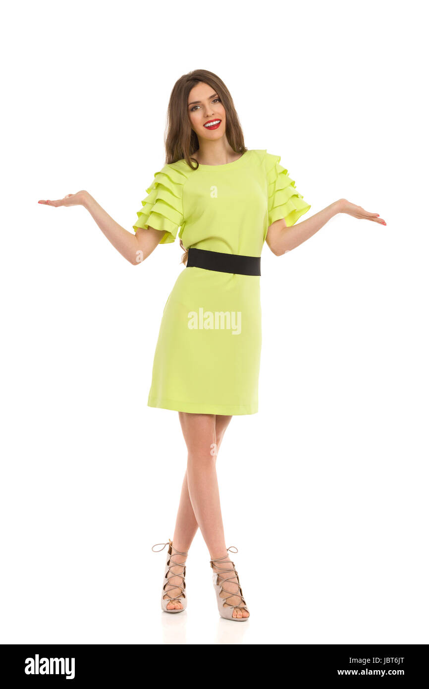 Schöne Frau im lindgrünen Kleid und high Heels posiert mit erhobenen Händen zu vergleichen oder zeigen etwas, Vorderansicht. Voller Länge Studio gedreht isola Stockfoto