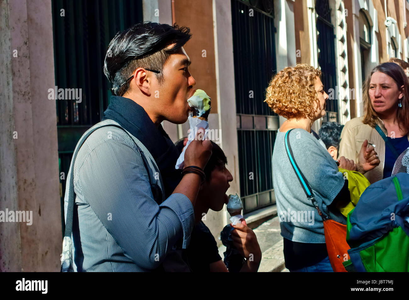Junger Asiat genießt es, Eis-Kegel im Freien in einer römischen Gasse Rom, Italien, Europa, Europäische Union, EU zu essen. Stockfoto