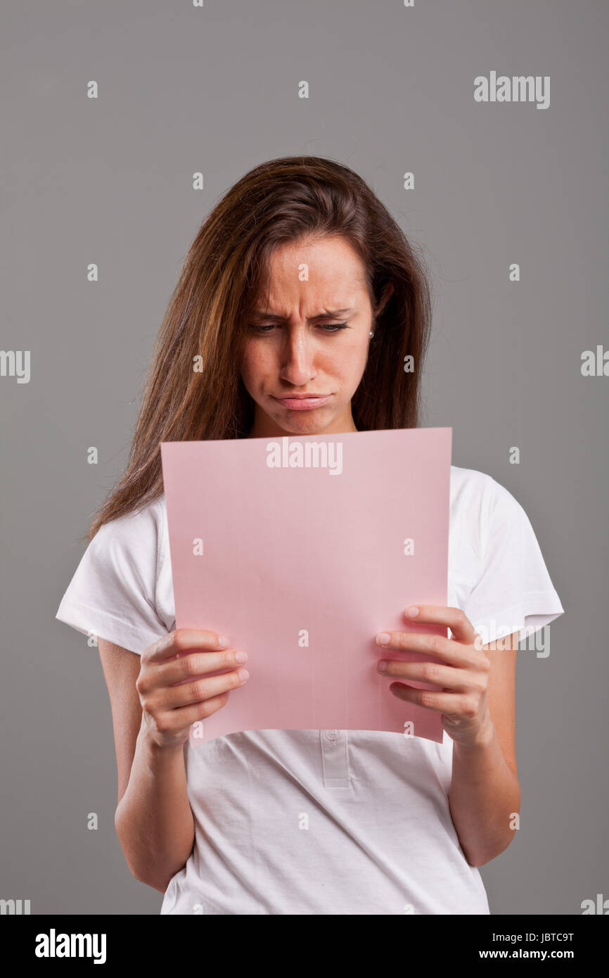 Mädchen schmollt, weil sie etwas Schlimmes an einem rosa Dokument vielleicht durch einen geliebten oder einen Geldverlust lesen Stockfoto