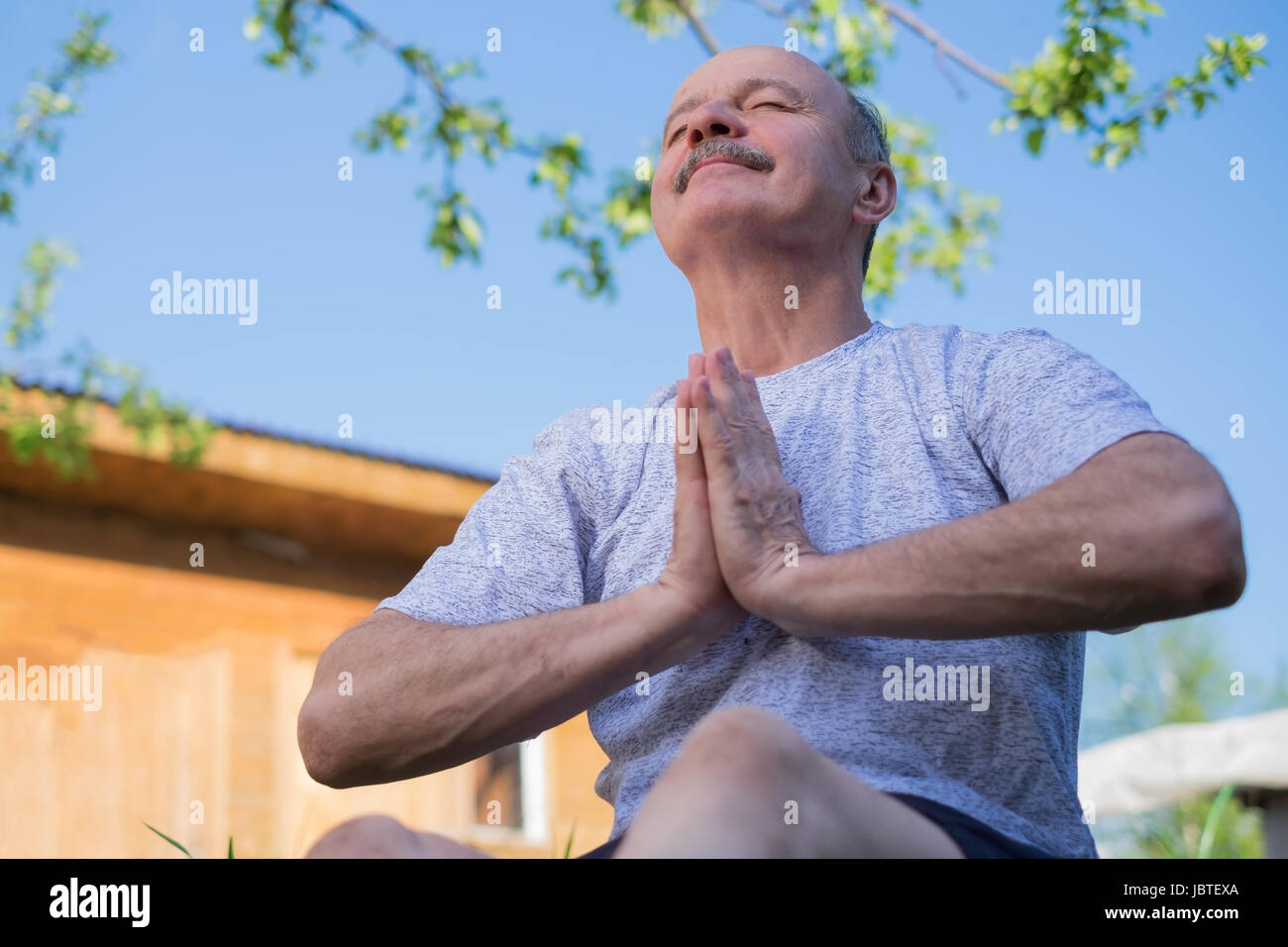 Ältere Mann mit Schnurrbart mit Namaste sitzen. Konzept der Ruhe und Meditation. Stockfoto