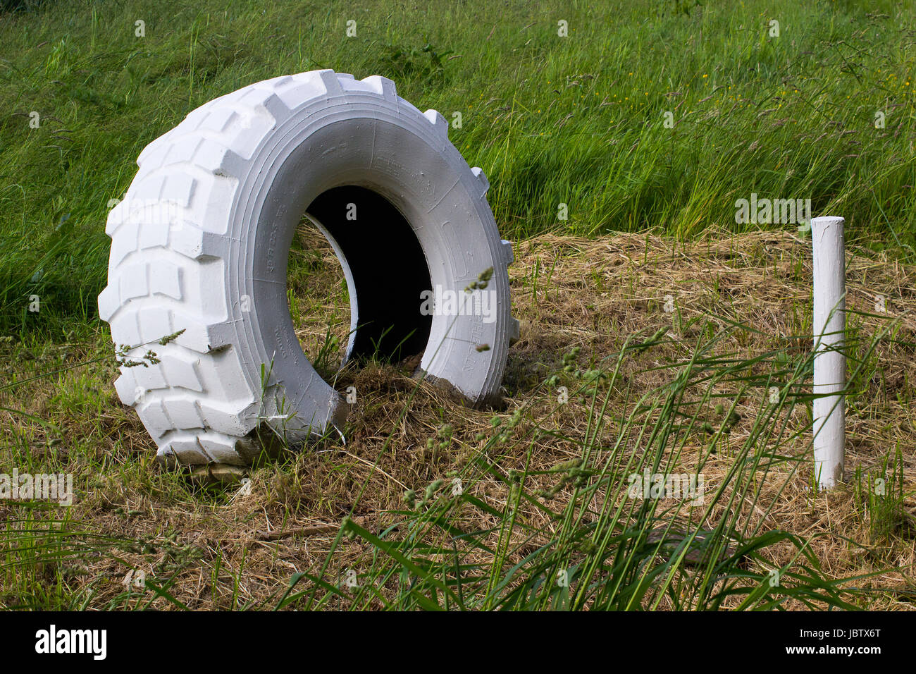 Eine große gebleicht Hinterachse Traktor-Reifen und einen hölzernen Pfahl verwendet als Marker in einem Bauernhof-Feld in Hampshire, England Stockfoto