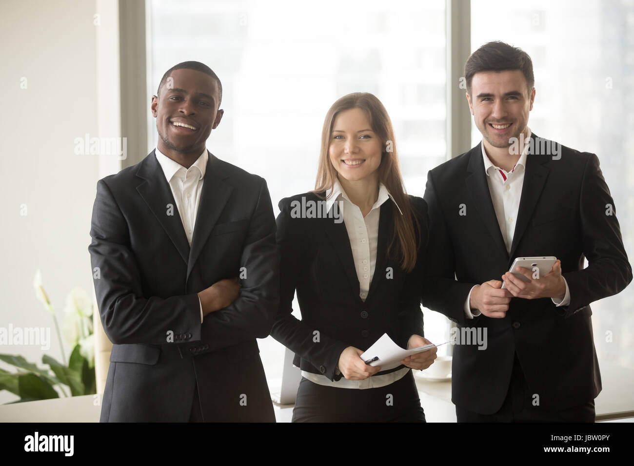 Fröhliche Geschäftsfrau in Abendgarderobe stehend zwischen zwei zuversichtlich Geschäftsleute posiert für die Kamera, multiethnischen Team Portrait, motivierte professional Stockfoto