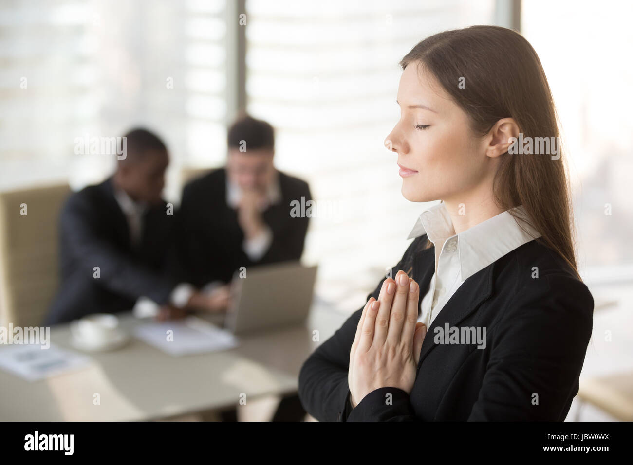 Junge schöne Geschäftsfrau genießt meditieren im Büro stehen mit geschlossenen Augen, Hände wie im Gebet zusammen, Stressabbau, Relief, ca zu halten Stockfoto