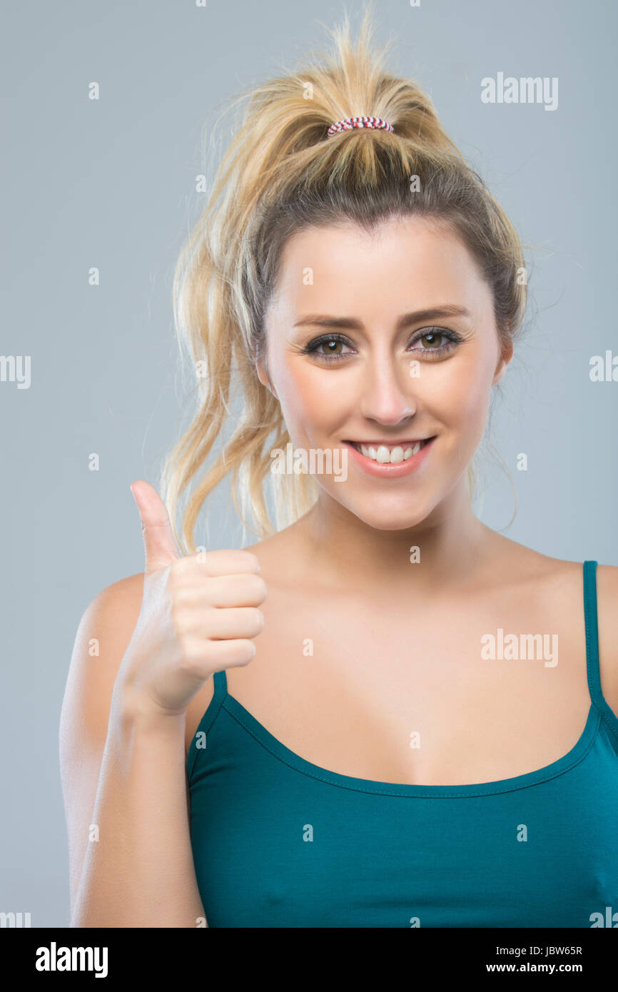 Glückliche junge, blonde Frau zeigt ein Daumen hoch Handzeichen Stockfoto