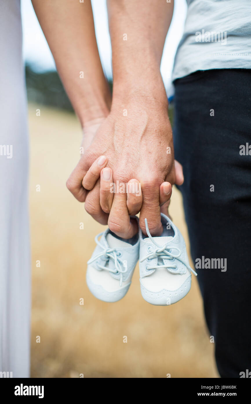 Paar Hand in Hand, Mann, hält Babyschuhe an Fingern, Nahaufnahme Stockfoto
