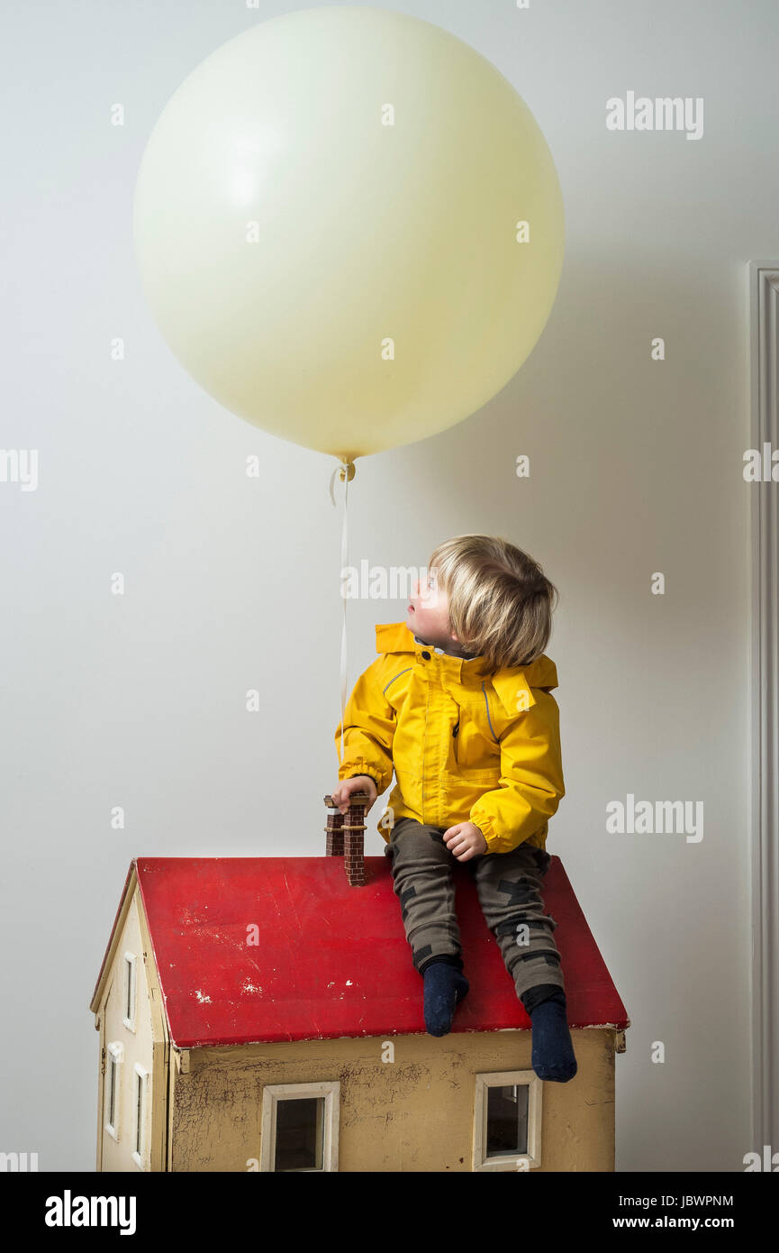Junge sitzt auf Puppenhaus blickte zu Ballon Stockfoto
