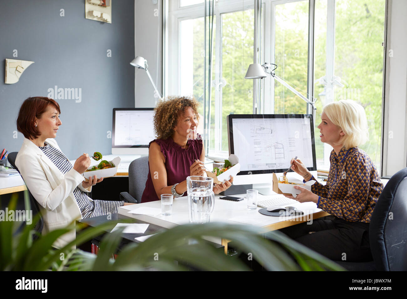 Drei Designerinnen mit Mittagessen im Büro arbeiten Stockfoto
