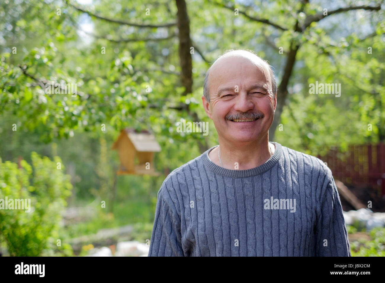 Reifer Mann sitzen im Garten in der Nähe von Apfelbaum im Land Stockfoto