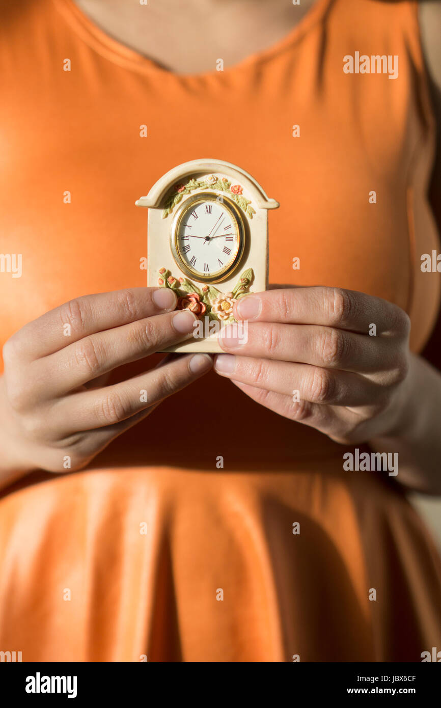 Nahaufnahme einer jungen Frau, die ein orange Kleid hält eine Vintage-Uhr Stockfoto