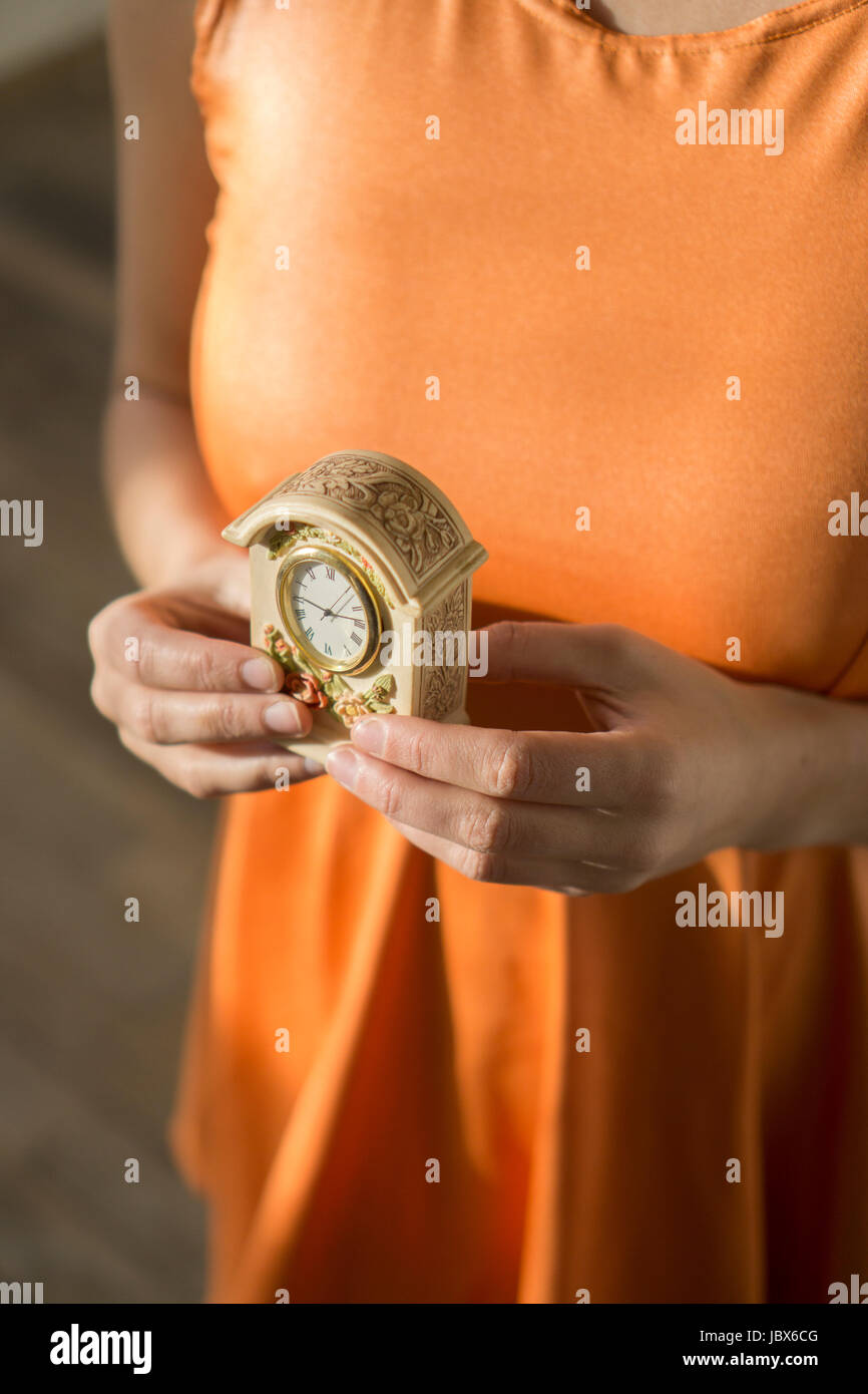 Nahaufnahme einer jungen Frau, die ein orange Kleid hält eine Vintage-Uhr Stockfoto