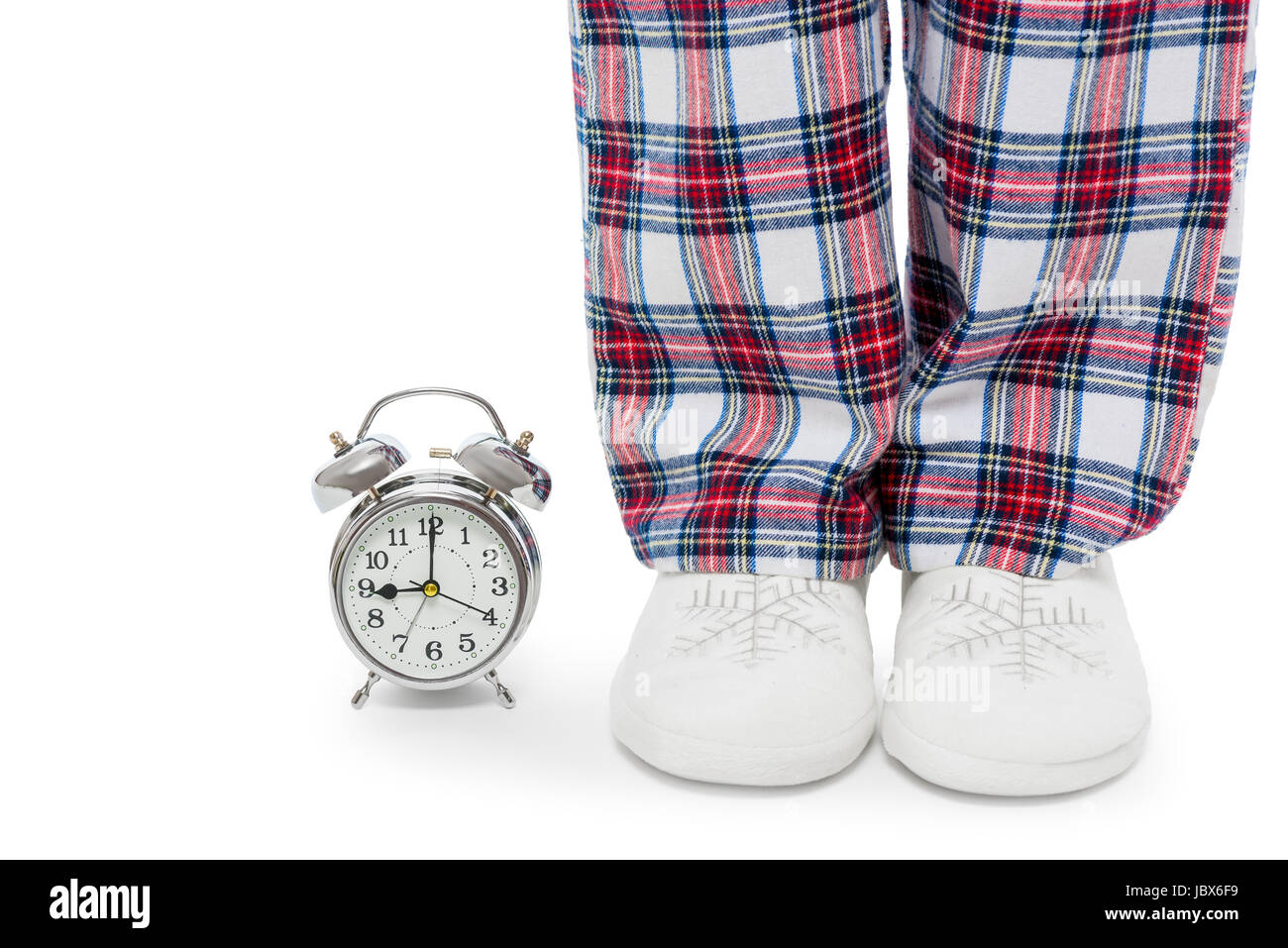 Wecker und weibliche Beine in Pyjama und Pantoffeln auf einem weißen Hintergrund closeup Stockfoto