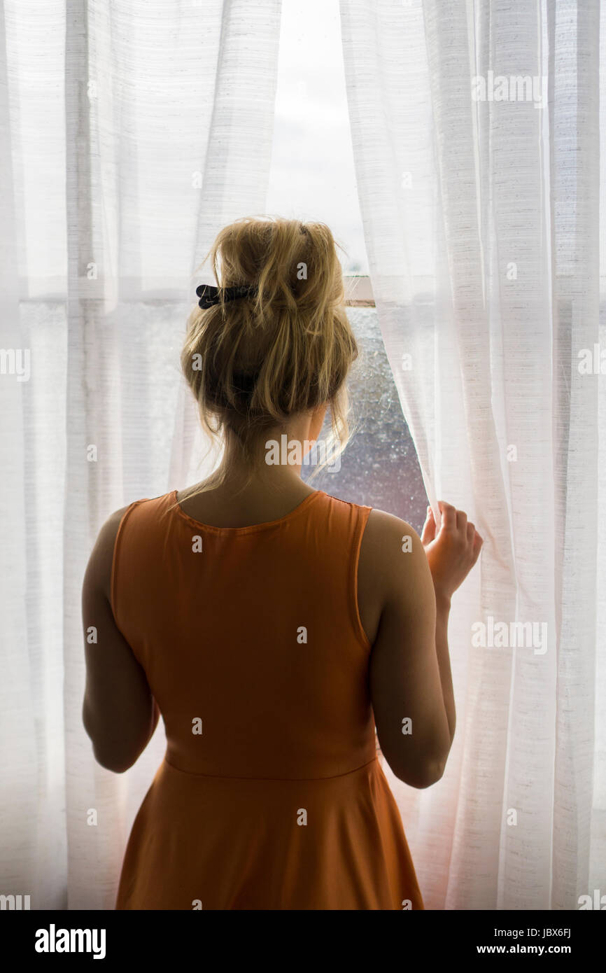 Rückansicht einer blonden kaukasischen Frau steht am Fenster, wegschauen Stockfoto
