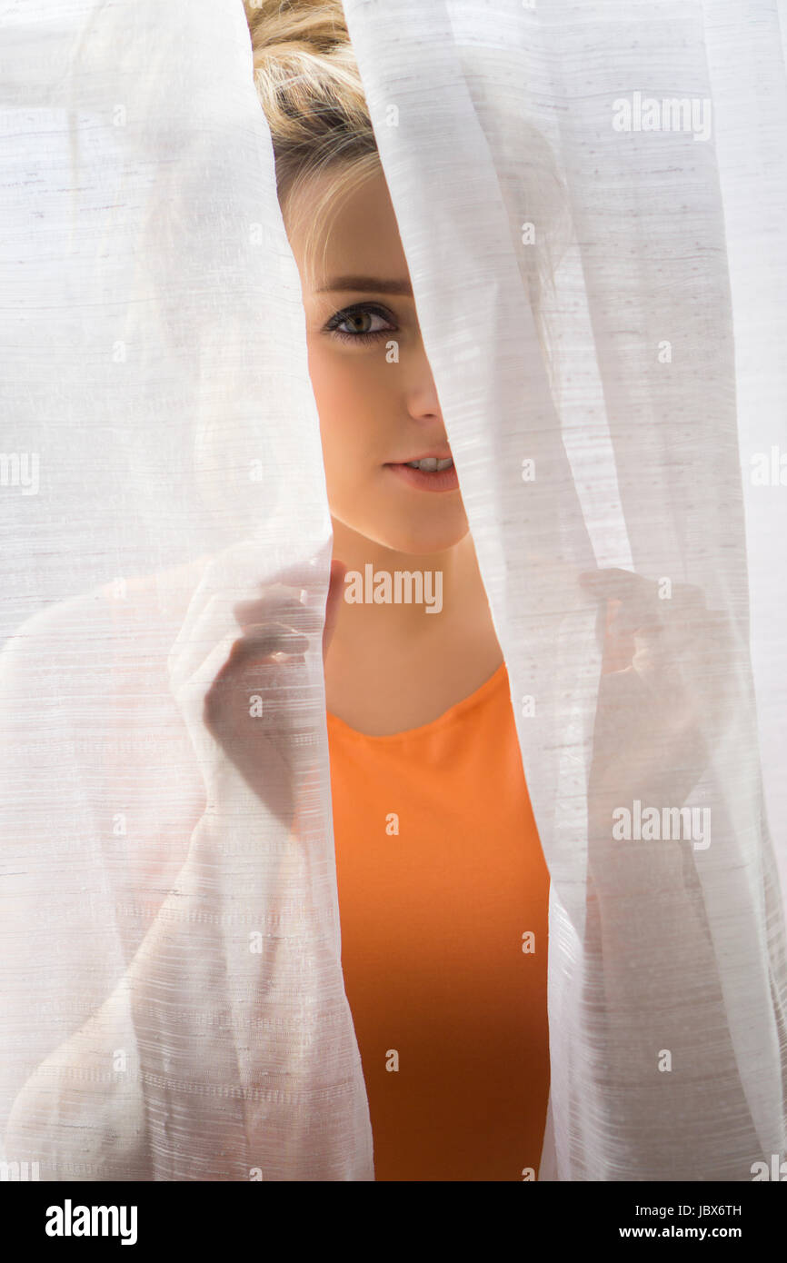 Porträt einer jungen Frau guckt hinter die Vorhänge Stockfoto
