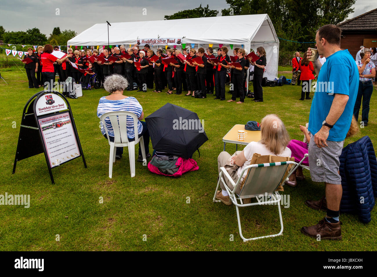 Lokale Leute sehen eine Community Choir Singing In The Rain am Maresfield Fete, Maresfield, East Sussex, UK Stockfoto