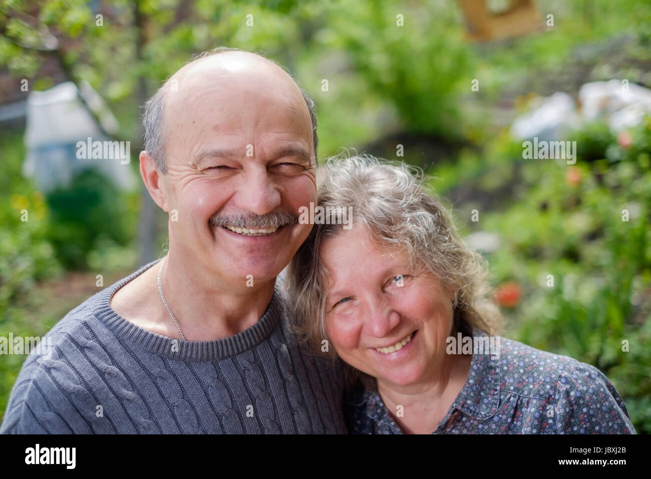 Reife Liebespaar auf der Rückseite Hof Garten in sonniger Tag. Sie Lächeln und schauen in die Kamera Stockfoto