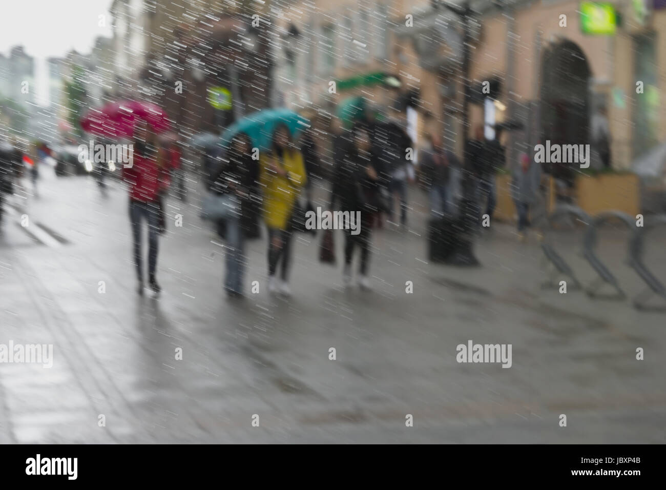 Abstrakte Stadtstraße durch Regentropfen auf Fensterglas gesehen. Mädchen in bunten Kleidern unter Sonnenschirmen auf Straße, unscharf Hintergrund. Moderne Jugend, Jahreszeiten Stockfoto