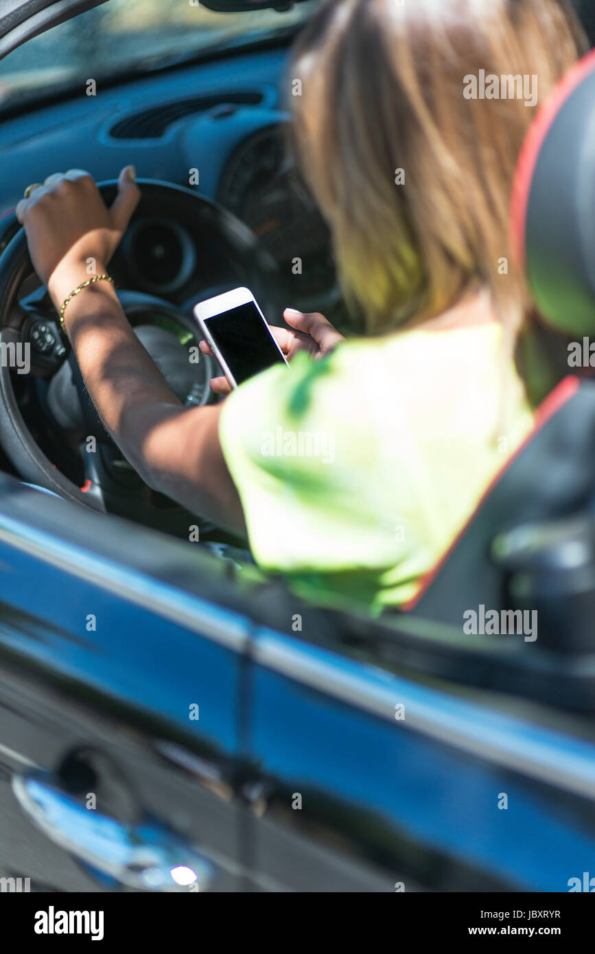 Junge Frau Autofahren Cabriolet mit ihrem Handy abgelenkt und gefährlich für den Verkehr um. Stockfoto