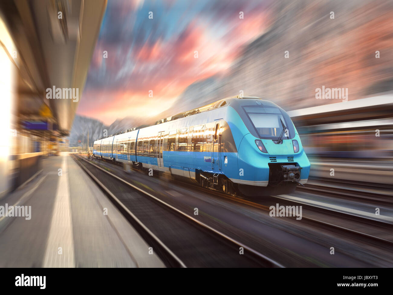 High-Speed-Zug in Bewegung am Bahnhof bei Sonnenuntergang. Moderne europäische intercity Zug auf dem Bahnsteig mit Motion-Blur-Effekt. Industri Stockfoto