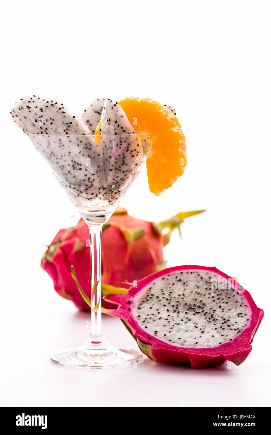 Keile ein Pitaya sortiert in ein Glas und dekoriert mit einer Mandarine Scheibe. Daneben eine halbierte, und dahinter eine ganze Frucht. Stockfoto