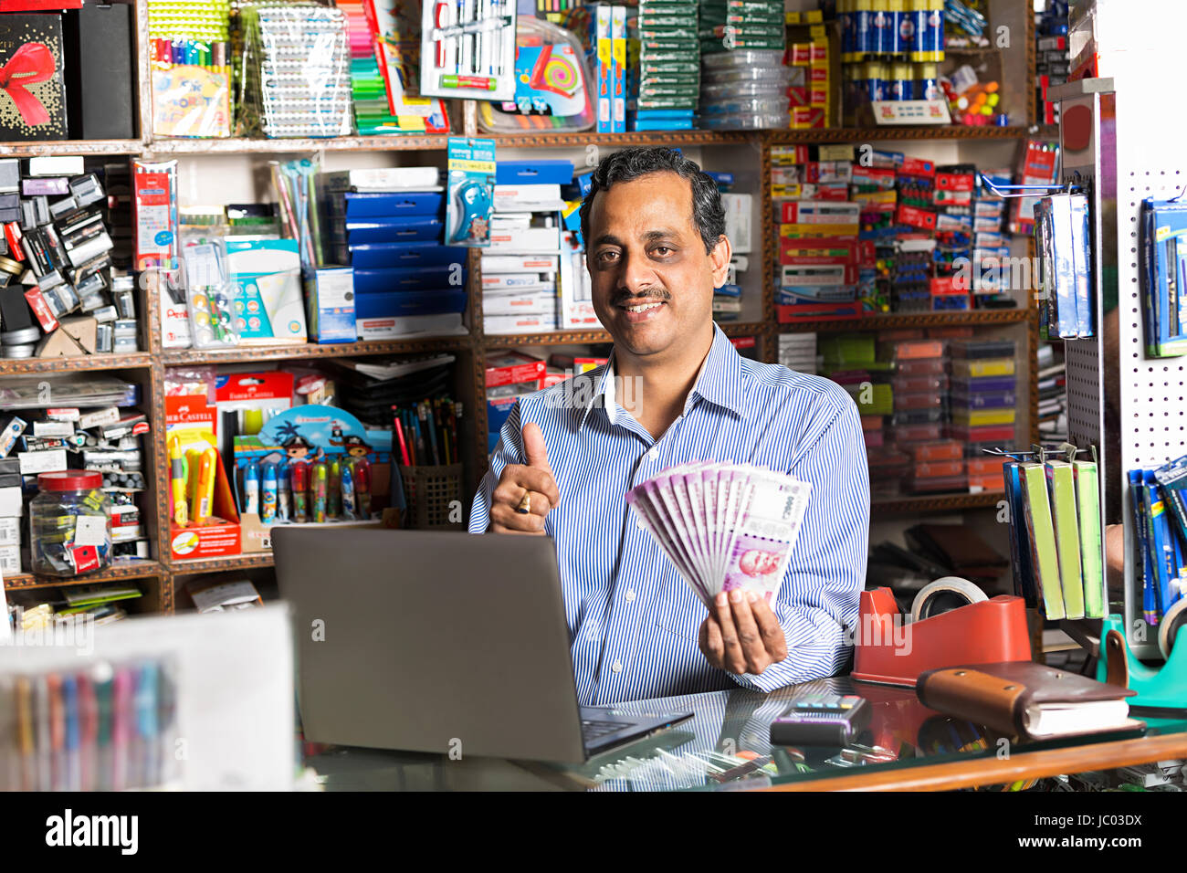 1 Indischer Ladenbesitzer Mann Daumen nach oben zeigt mit Geld Rupien Zähler stehen Stockfoto