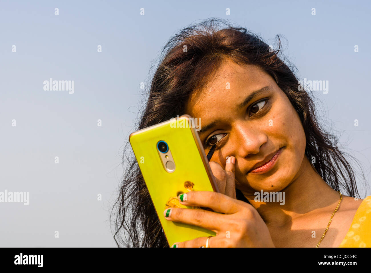 Eine junge Frau ihr Make-up, mit einem Mobil Telefon als Spiegel auf den Strand von Ganga Sagar Stockfoto